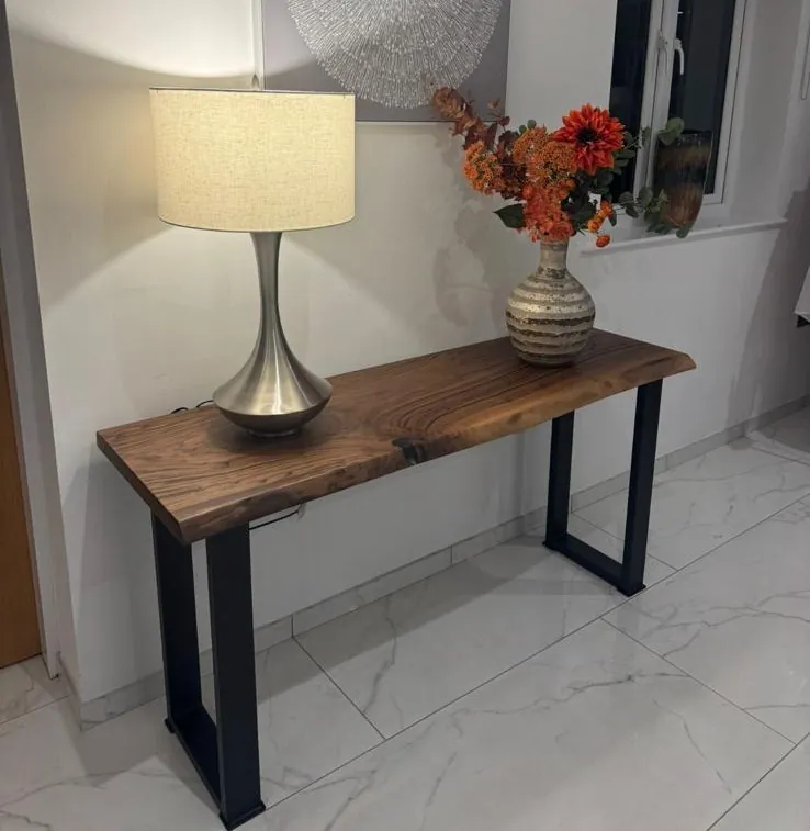Una consolle in noce con una lampada e un vaso di fiori contro una parete bianca
